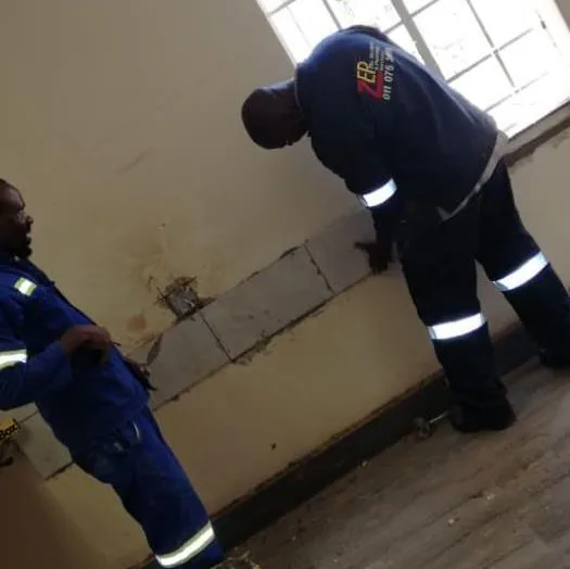 Two technicians in navy overalls inspecting an interior wall