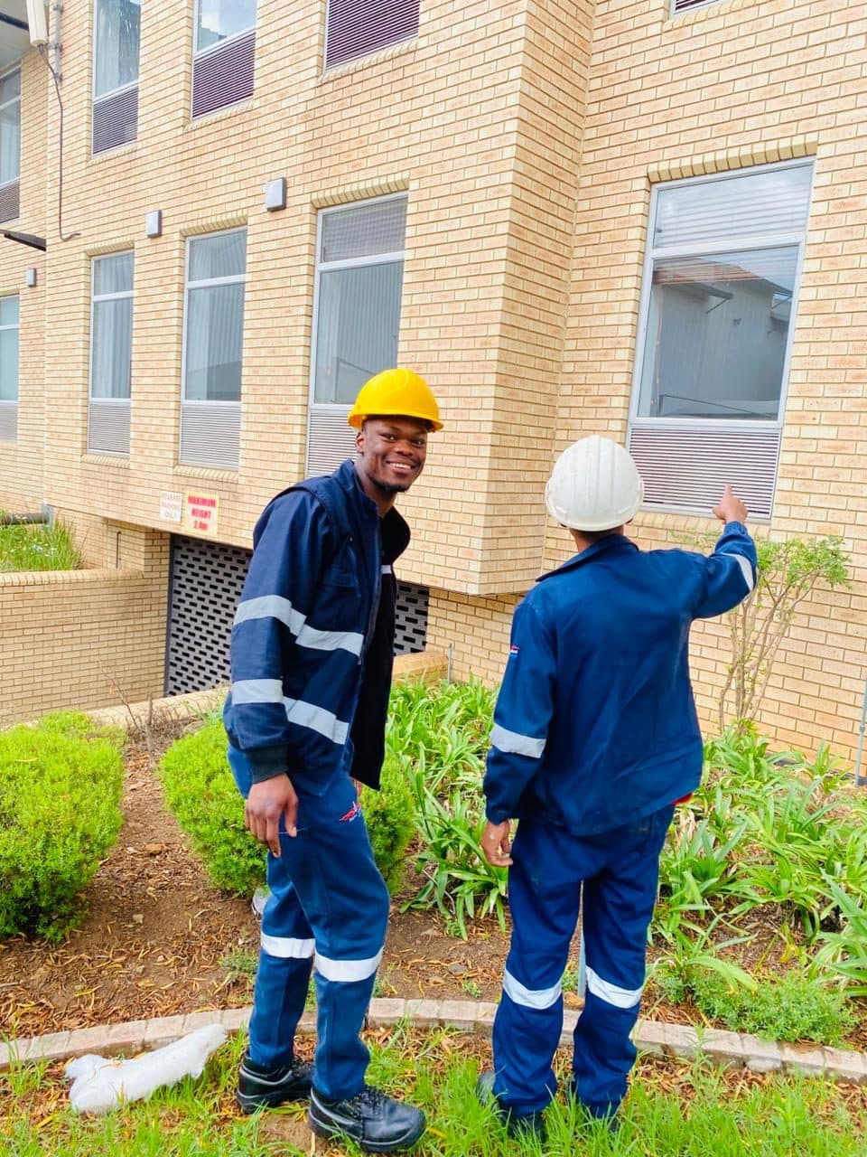 Two ZEPS technicians in hard hats at a brick building, one smiling